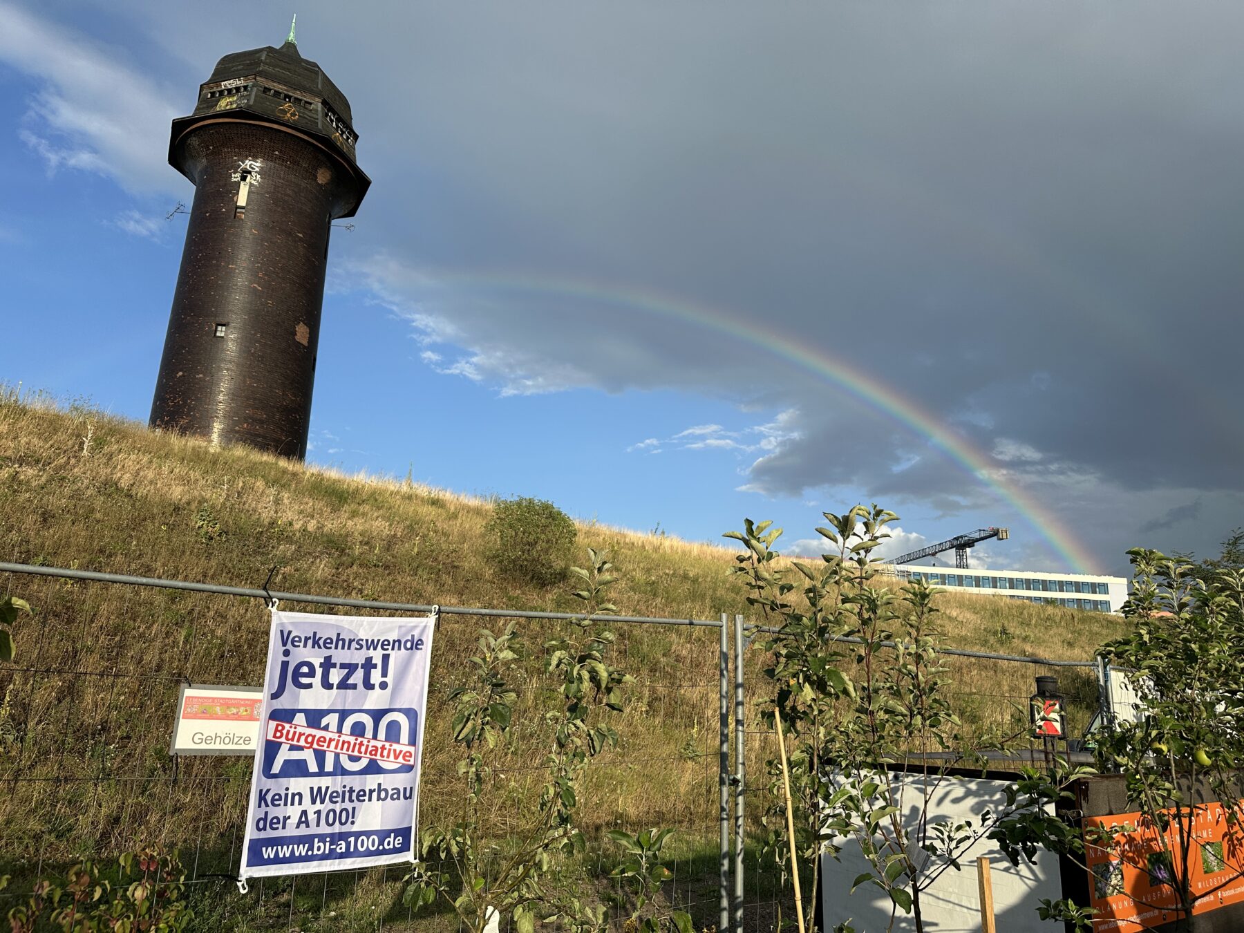 Plakat der Bürger*innenInitiative A100 vor dem Wasserturm am Ostkreuz mit Regenbogen am Horizont